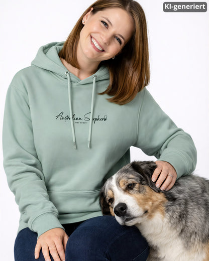 KI-generiertes Modelbild: Frau trägt Hoodie in Aloe mit Brustmotiv "Australian Shepherd. Was sonst?" und sitzt neben ihren Australian Shepherd.