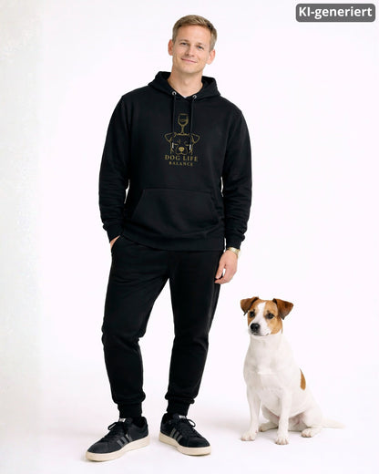 KI-generiertes Modelbild: Mann trägt schwarzen Hoodie mit goldenem Dog-Life-Balance-Motiv mit Hundekopf und Weinglas neben einem Jack Russell.