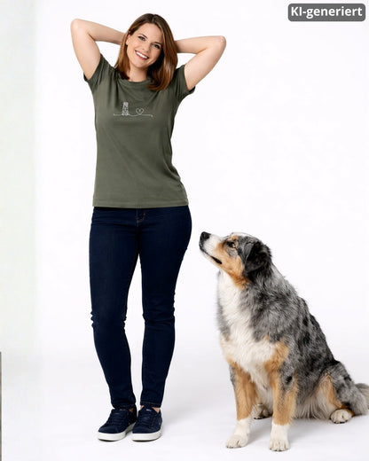 KI-generiertes Modelbild: Frau trägt khakifarbenes Shirt mit Australian-Shepherd-Linienmotiv mit Herz und steht neben einem Australian Shepherd.