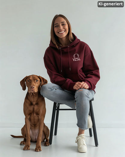 KI-generiertes Modelbild: Frau trägt Burgundy-Hoodie mit Vizsla-Brustmotiv „VZSL“ und sitzt neben einem Vizsla.