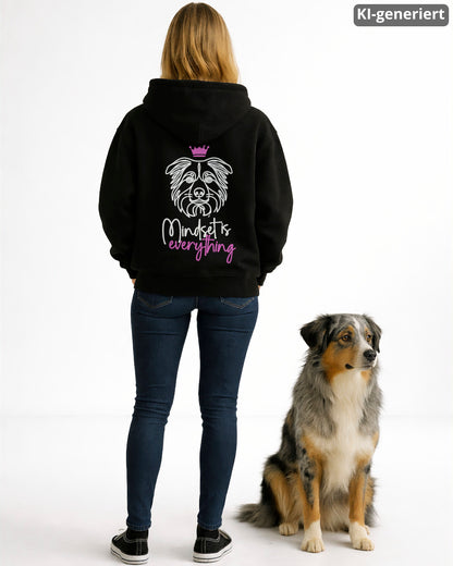 KI-generiertes Modelbild: Frau trägt schwarzen Hoodie mit „Mindset is everything“-Rückendruck mit Australian-Shepherd-Kopf und Krone neben einem Australian Shepherd.