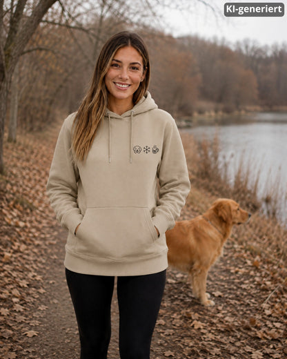 KI-generiertes Modelbild: Frau in einem Hoodie in Desert Dust mit kleinem Wintermotiv auf der Brust, im Hintergrund steht ein Golden Retriever an einem Seeufer.