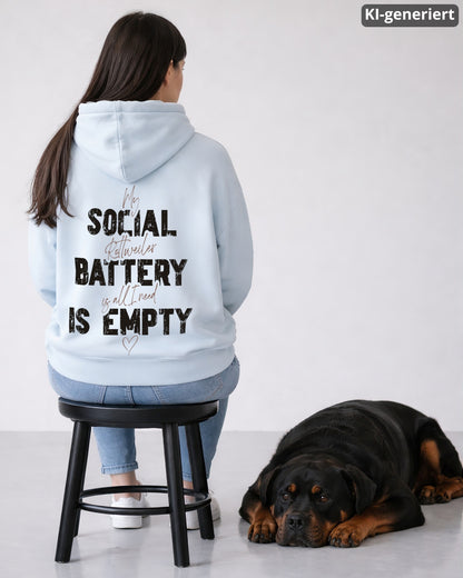 KI-generiertes Modelbild: Frau sitzt mit dem Rücken zur Kamera auf einem Hocker und trägt einen Oversized Hoodie in der Farbe Blue Ice mit großem Backprint-Motiv „Social Battery is empty“, daneben liegt ein Rottweiler entspannt auf dem Boden.