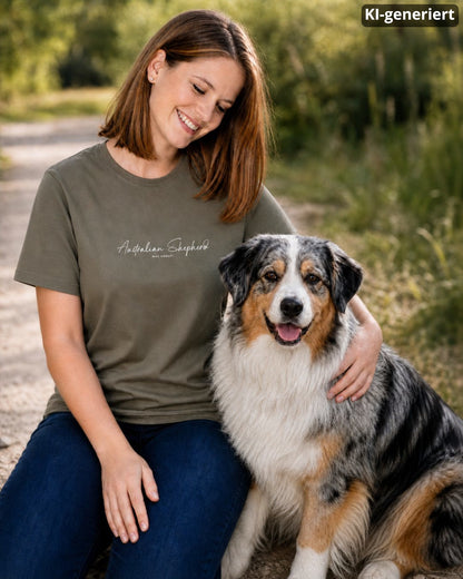 KI-generiertes Modelbild: Frau trägt khakifarbenes Shirt mit Australian-Shepherd-Schriftzug „Was sonst?“ und kniet neben einem Australian Shepherd.