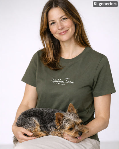 KI-generiertes Modelbild: Frau trägt khakifarbenes Shirt mit Yorkshire-Terrier-Schriftzug „Was sonst?“. Ein Yorkie liegt auf ihr.